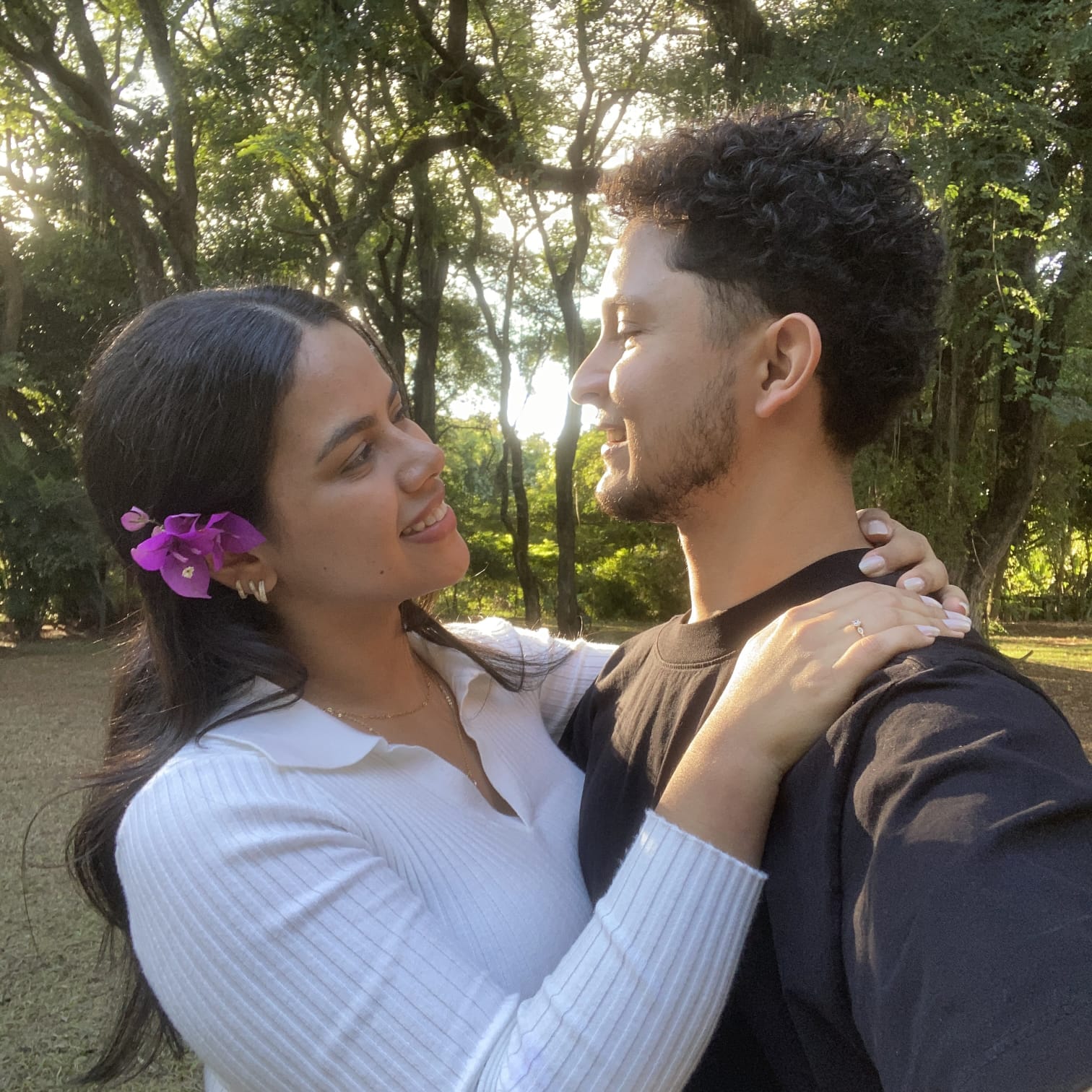 Andressa e Matheus se olhando e sorrindo ao sol, entre as árvores